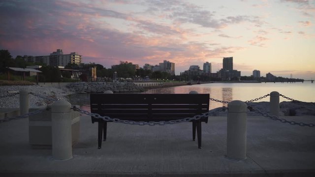 Bench overlooking a rocky beach with pink sunrise in a small city at dawn.