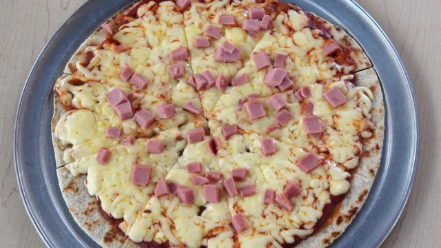 Sliced ham pizza on wooden table.