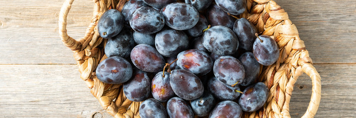 Ripe plum. Lots of plums in a basket on a gray wooden table. Blue plums close-up. Healthy fruits. Banner	