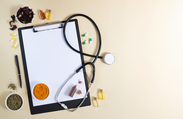 Blank clipboard with stethoscope, various healthy herbs, spices, capsules and oils top view