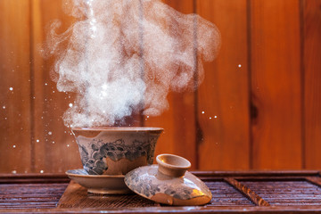 Traditional chinese painted clay tea brewing cup with cloud of steam and splashing hot water on wooden background