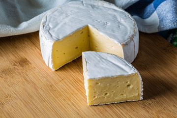 Fresh Brie cheese and a slice close up on wooden board