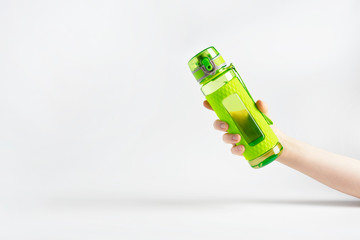 Woman hand holding green plastic fitness bottle flask on plain white gray background. Copy space for text