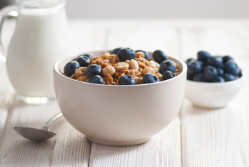 Breakfast with granola and blueberry, milk with orange juice and baked toasts on the white wooden table close-up