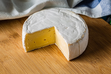 Fresh Brie cheese without cut slice on wooden board