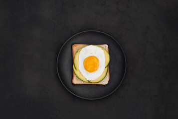 Healthy breakfast toasts with avocado and fried egg on the black stone background flat lay mock-up with copy space