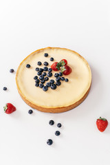 Whole cheesecake with fresh strawberries and blueberries on a white table.