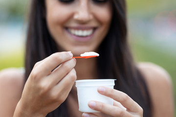 Beautiful young woman smiling while eating an ice cream standing in the street.