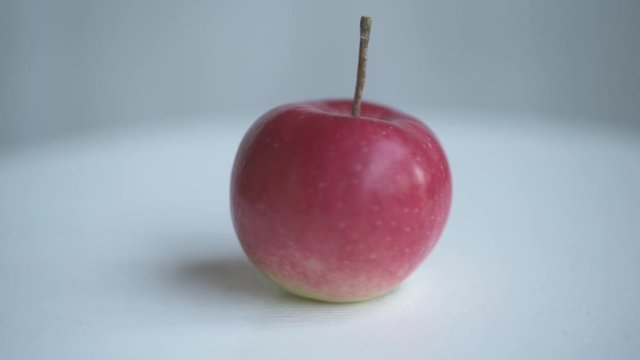 Red apple rotate on white table. Loopable moving image.