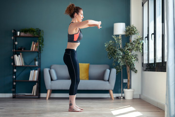 Attractive sporty young woman doing hypopressive exercises in living room at home.