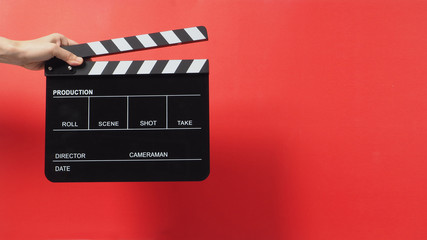 Hand is holding black clapper board on red background.