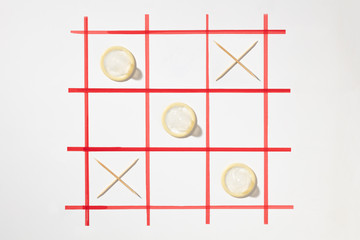 Tic-tac-toe game. Elements in the form of condoms and toothpicks. Сondoms and toothpicks in the form of noughts or zero and crosses on a checkered field.  Сoncept of choosing birth control.