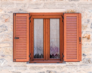 natural wood window frame with shutters on stonewall