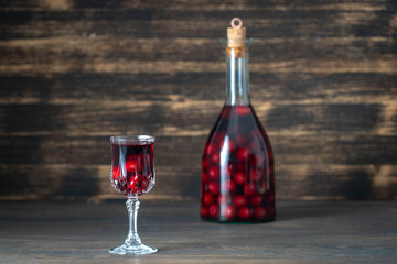 Homemade tincture of red cherry in a glass bottle and a wineglass on wooden background, Ukraine