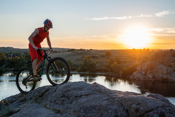 A cyclist rides a mountain bike on the rocks during sunset, a copy of the free space.