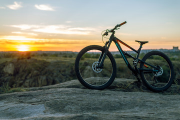A full suspension mountain bike stands on a rock against the backdrop of a sunset. MTB. Cycling.