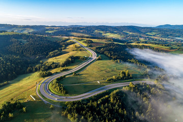 Poland. Winding switchback road from Krakow to Zakopane, called Zakopianka, near Rabka and Chabowka. Aerial view in sunrise light with morning fog. Far view of Tatra mountains in the background