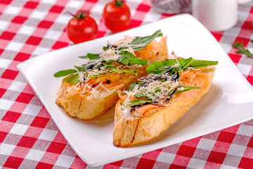 Italian Appetizer Bruschetta with Salmon, parmesan, balsamic vinegar and fresh arugula on white plate in restaurant background,