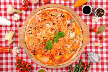 Pizza with seafood, mozzarella, mussels, octopus, squid, salmon, shrimp, cheeseand, fresh rucola and tomatoes sauce, served on a wooden board for a dinner in italian restaurant background, top view. 