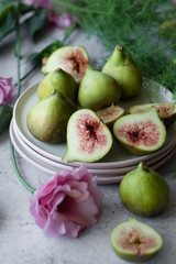 Ripe whole half and sliced figs among flavored green leaves of herbs and colorful flowers