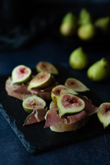 Bread with ham and fresh figs served on a black stone plate.