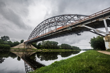 Metal bridge with lattice girders. Landscape with an iron bridge across the river. Cloudy sky reflects in river waters. Landscape of Moscow channel