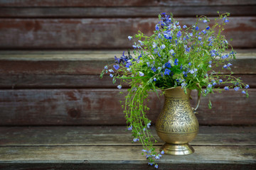 Fototapeta na wymiar A bouquet of blue Veronica chamaedrys in a brass vase on an old wooden background. Selective focus