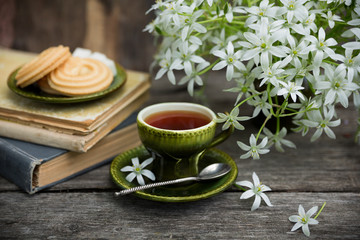 A cup of tea vintage on the background of a bouquet with white flowers, old books, cookies and an...