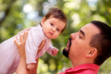Father raising in arms infant daughter, talking to her, outdoors in sunny summer or autumn day....