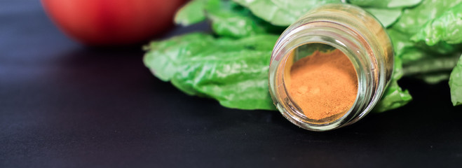 Primer plano de un pequeño pote de cúrcuma abierto junto a una lechuga fresca como fondo. Foco selectivo sobre al pote de condimento. 