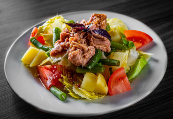 Salad nicoise. Tuna, with green beans, tomatoes, potatoes and a vinaigrette mustard dressing in white plate on black wooden table background