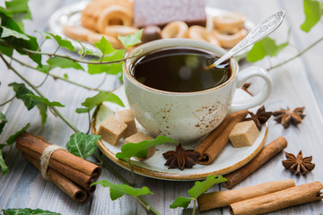 White cup of coffee with cinnamon and aniseed stars on a light wooden background with green ivy. Selective focus