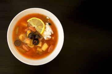 Slavic Solyanka soup in a white bowl on dark wooden background with copy space. Top view. Famous traditional Ukrainian and Russian saltwort soup with lemon.