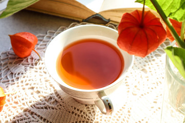 A Cup of tea with physalis and a book on a lace napkin, top view, close-up