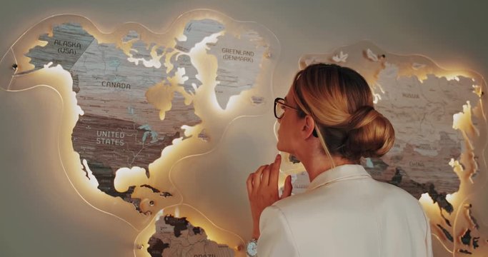 woman in white business suit looking at the world map on the wall in the room