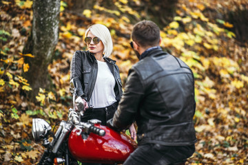 Fototapeta na wymiar Pretty couple near red motorcycle on the road in the forest with colorful blured background