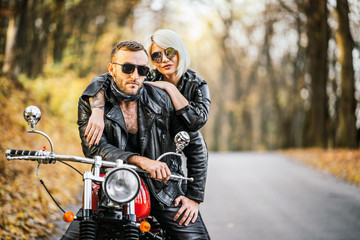 Pretty couple near red motorcycle on the road in the forest with colorful blured background