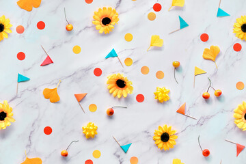 Abstract Fall seasonal background with yellow flowers, Autumn gingko leaves, paper confetti and toothpick flags. Flat lay on white marble table.