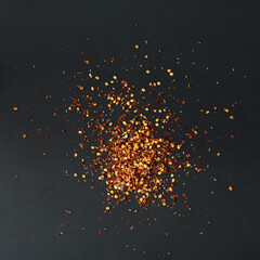 Pile crushed red cayenne pepper, a dried chili flakes and seeds on black background. Homemade...