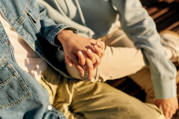 Close up of hands of lesbian couple. Two girls holding their hands, sitting on the bench on a sunny...