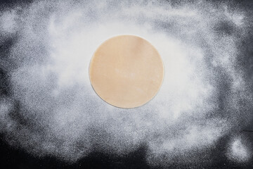 Pizza dough with flour on dark table