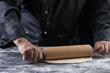 Man hands keep rolling pin with dough on dark table, top view