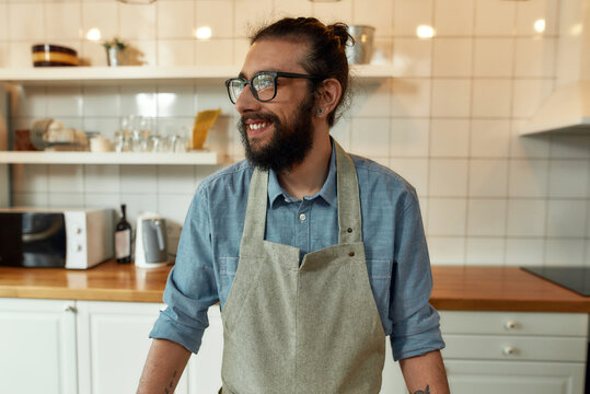 Portrait Of Young Man, Italian Cook In Apron Smiling Aside While Getting Ready To Prepare Healthy Meal With Vegetables In The Kitchen. Cooking At Home Concept