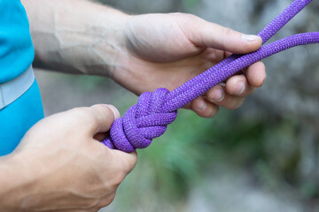 Male hands tying figure-eight knot using purple climbing rope. Active hobby, sportive leisure