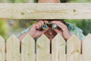 Curious neighbor stands behind a fence and watches - obrazy, fototapety, plakaty