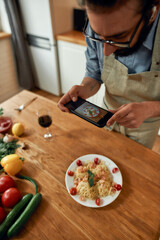 Delicious meal. Young man, cook taking picture of garlic butter shrimp pasta, meal decorated with basil and cherry tomatoes. Cooking at home, Mediterranean cuisine concept
