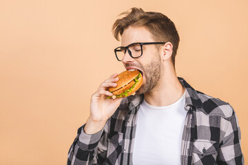 Young man holding a piece of hamburger. Student eats fast food. Burger is not helpful food. Very hungry guy. Diet concept. Isolated over beige background.