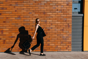 Young cheerful businesswoman, wearing all black, walking on the street, smiling.