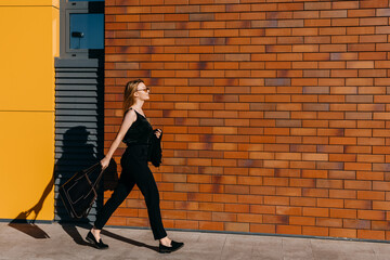 Young happy businesswoman, wearing all black, walking on the street, smiling.