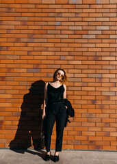 Young businesswoman standing on a brick wall background on the street.